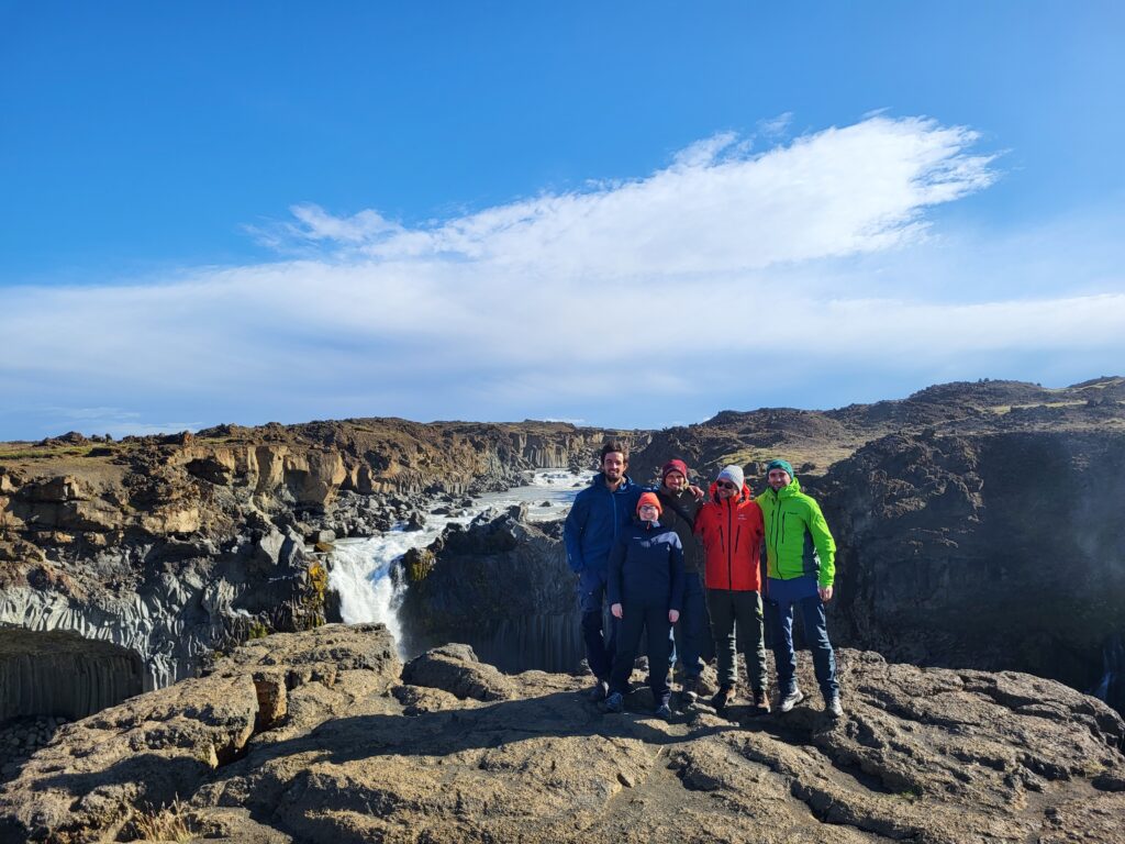 The NORDQUA Secretariat standing together on a rock ledge in front of the Aldeyjarfoss waterfall